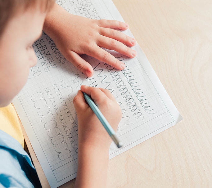 Young boy applying pencil to paper, learning how to make shapes